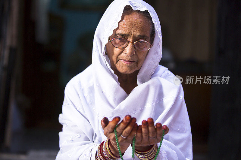 Senior Muslim Woman praying, with prayer beads beads in her hands